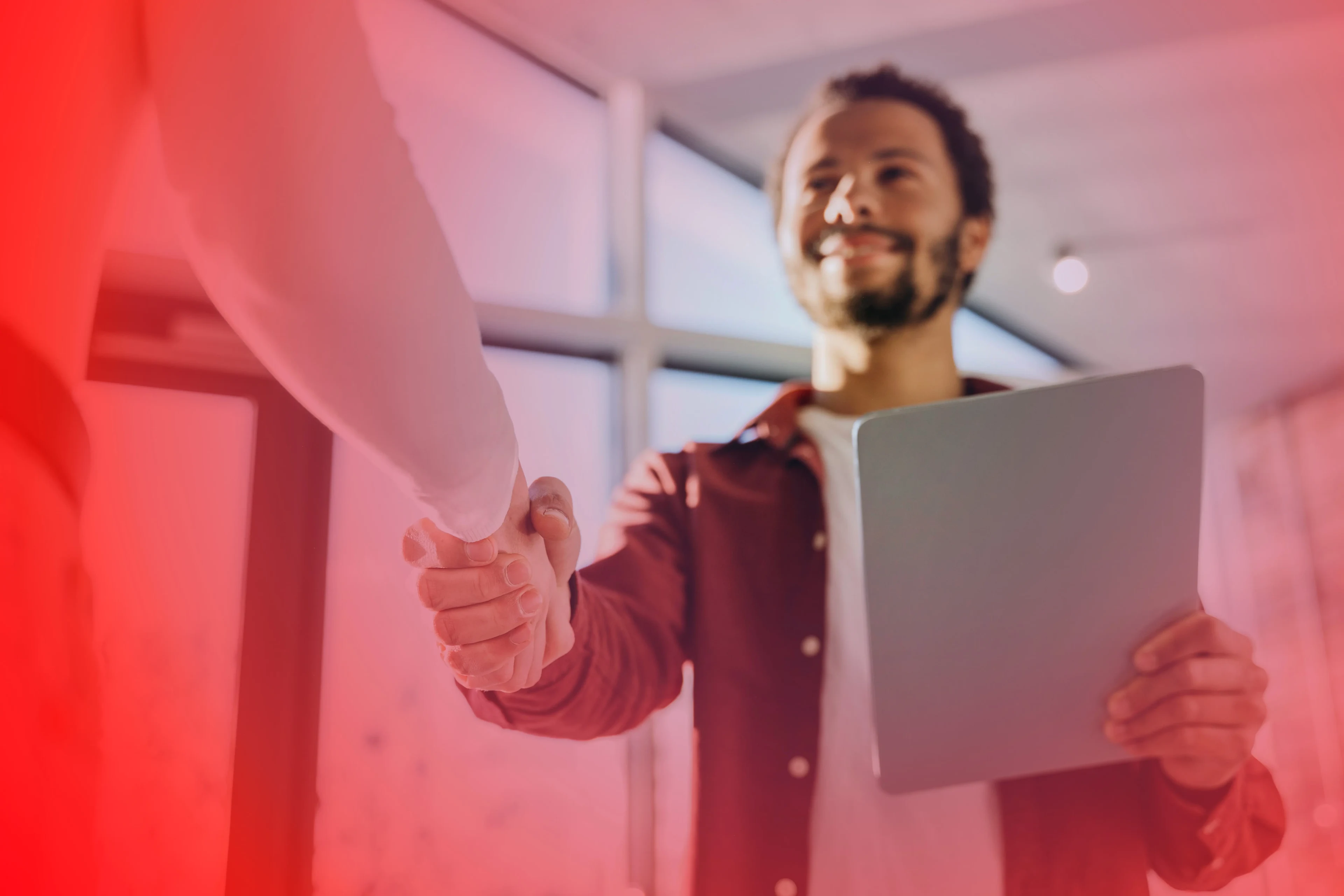 Zwei Geschäftsleute geben sich die Hand in einem modernen Büro, während einer ein Tablet hält, symbolisch für eine erfolgreiche Vereinbarung oder Partnerschaft.